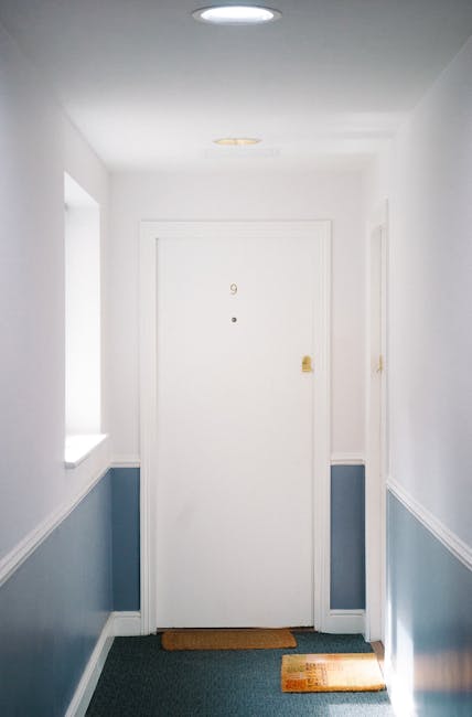 A low-angle view of a corridor with a carpeted floor, featuring striped wallpaper on both sides and closed white wooden doors. The carpet appears clean and well-maintained, with a uniform texture and 